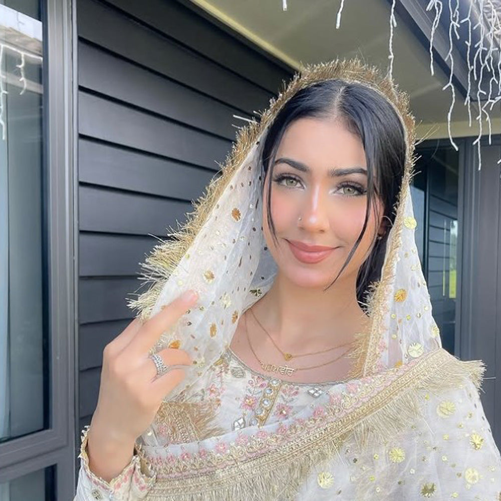 Girl in white Punjabi suit with chunni on her head, wearing gold Punjabi name necklace