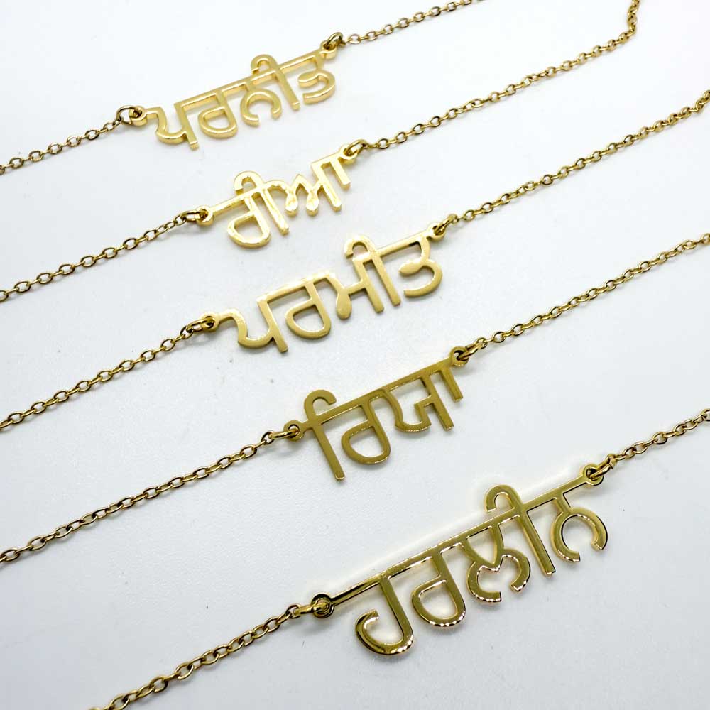 Flat lay of five custom Punjabi name necklaces in gold, handmade and lined up on neutral background