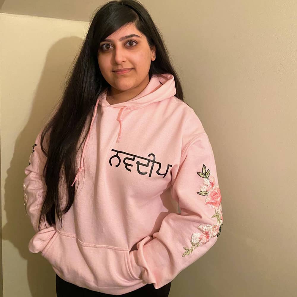 Girl in light pink personalised Punjabi hoodie with black Gurmukhi name and pink floral embroidery