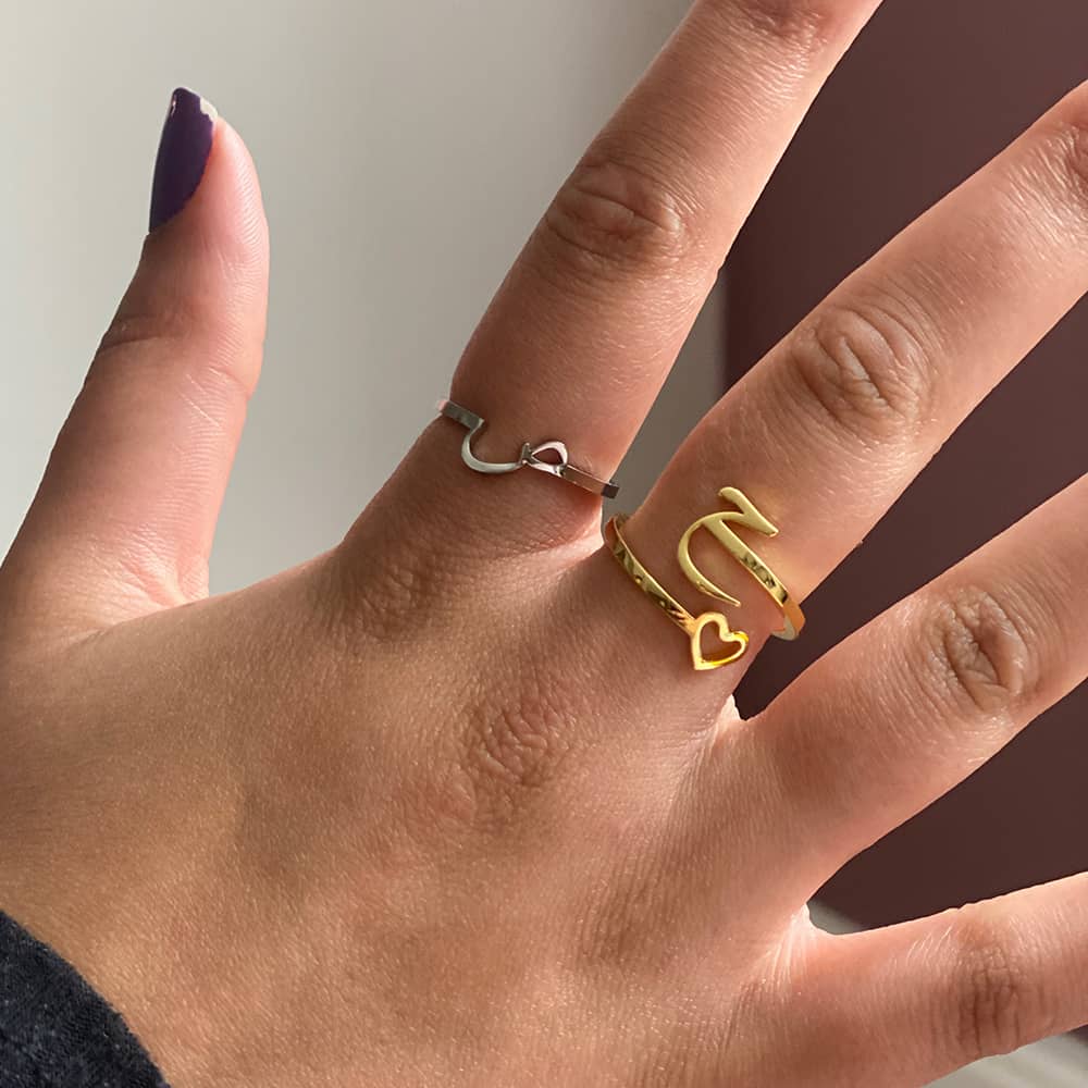 woman wearing arabic initial ring in silver and a gold twisted arabic initial ring with heart