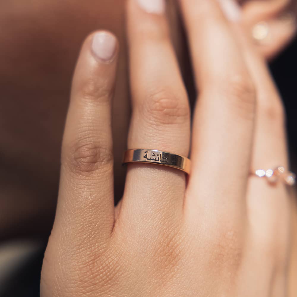 woman wearing rose gold band ring with black engraving of arabic name on outside for couples