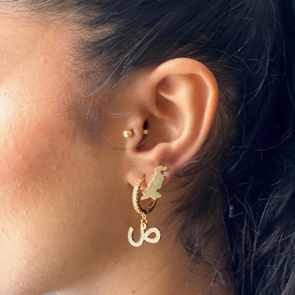 woman wearing hoop earrings with initial in arabic and a pakistan map stud earring in gold plating