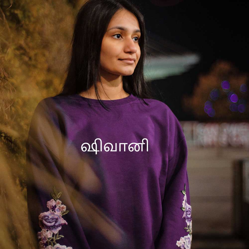 woman wearing plum purple sweatshirt with white name in tamil and purple floral embroidery