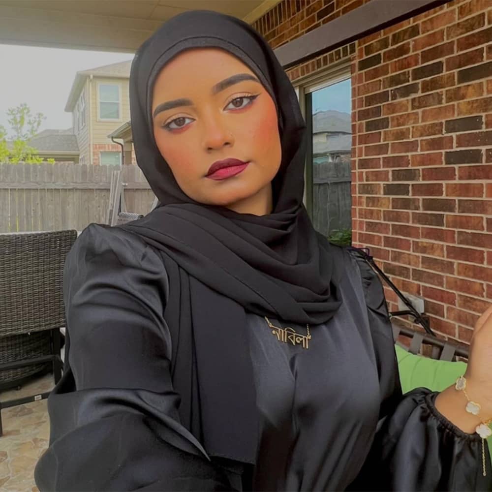 Influencer Nabila wearing Bangla name necklace in gold with black dress and black hijab