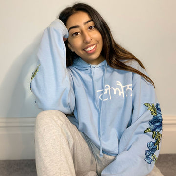 woman wearing punjabi hoodies with name in punjabi on light blue hoodie and blue floral embroidery