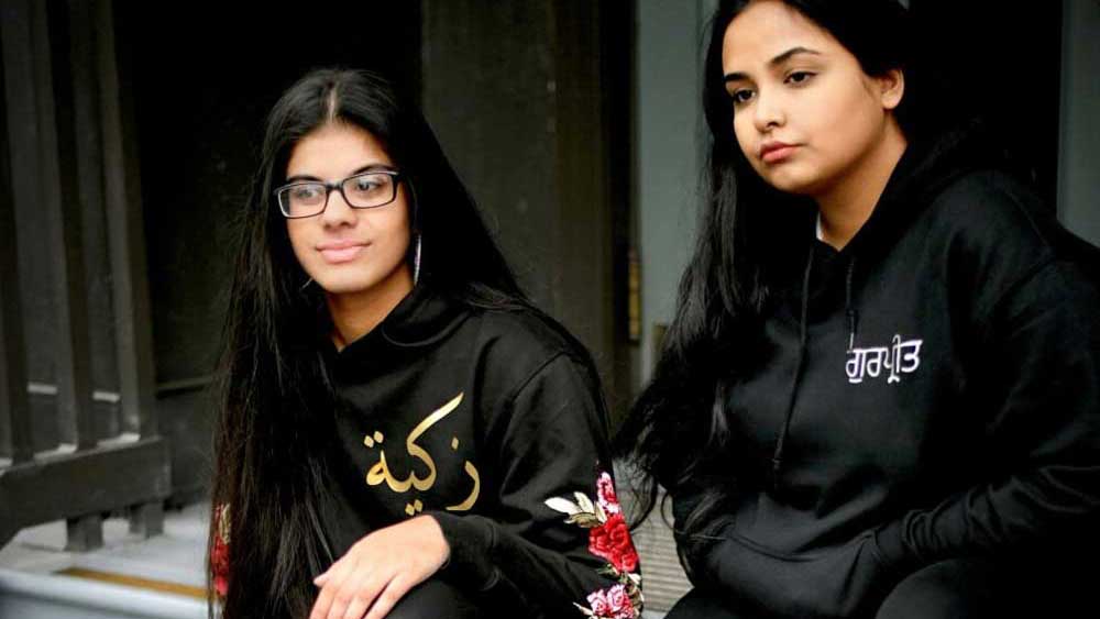 sisters wearing matching black hoodies with name in arabic and punjabi with floral sleeve embroidery