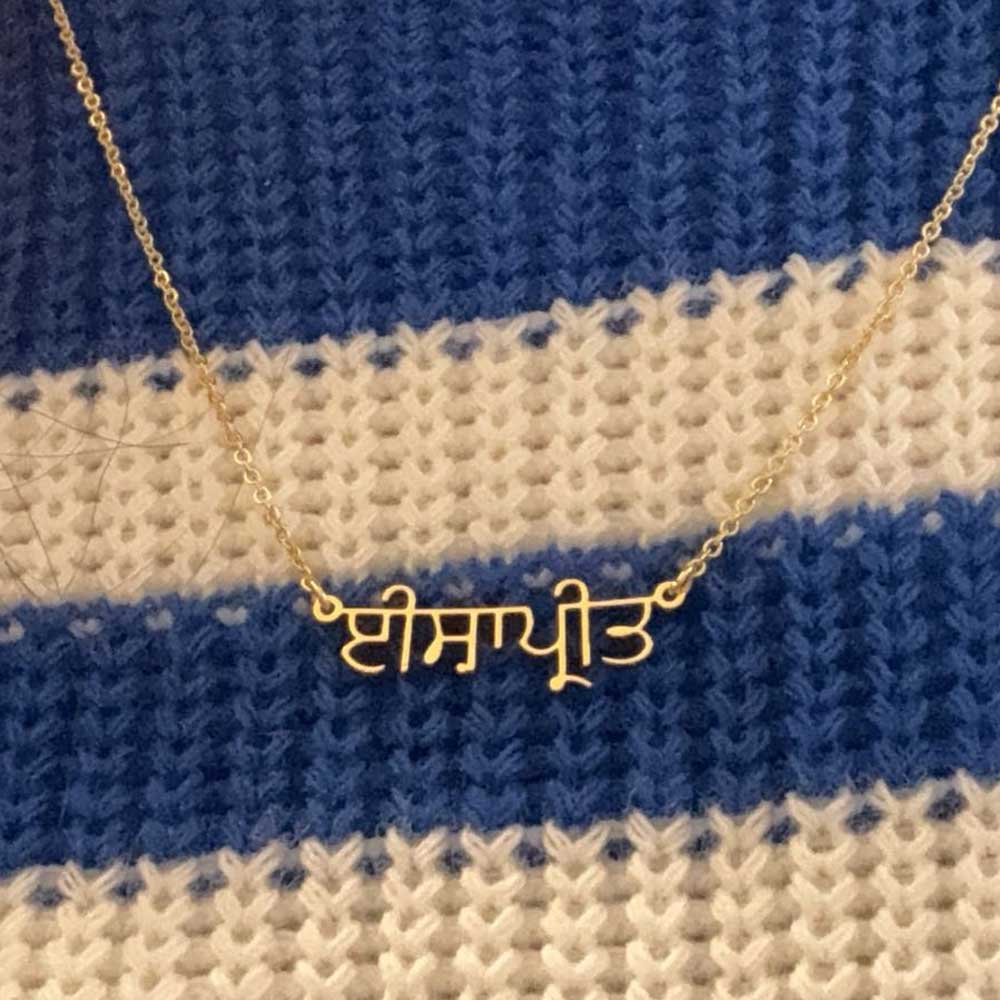 Close-up of woman’s neck with Punjabi name necklace, styled with blue and white knit jumper
