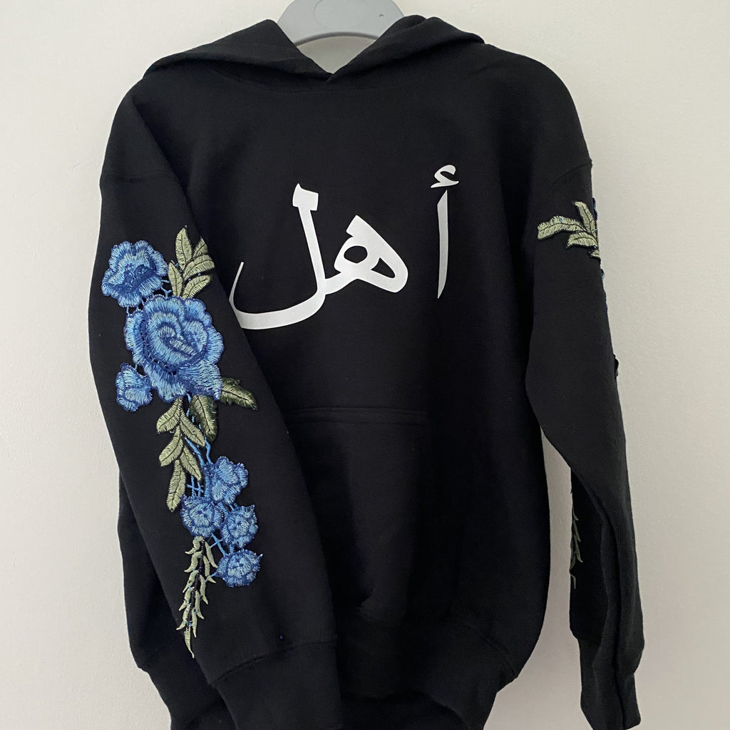 Customer Order photo - black kids hoodie with white arabic name (font 1) across the chest and blue floral sleeve emrboidery
