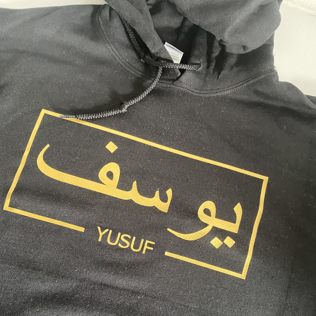 black hoodie with metallic gold design Arabic and English name across chest