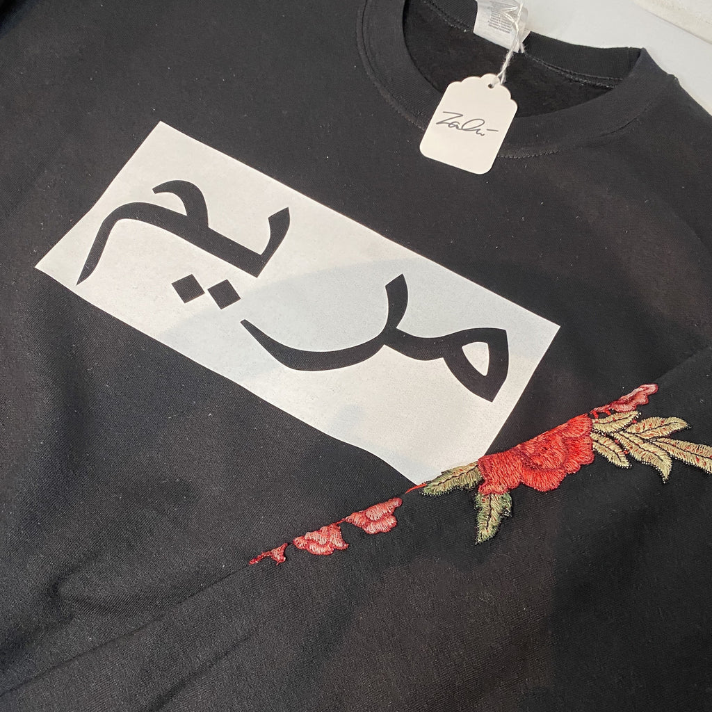 Customer Order Photo - black sweatshirt with white rectangle across the chest and black name inside rectangle and red floral sleeve embroidery