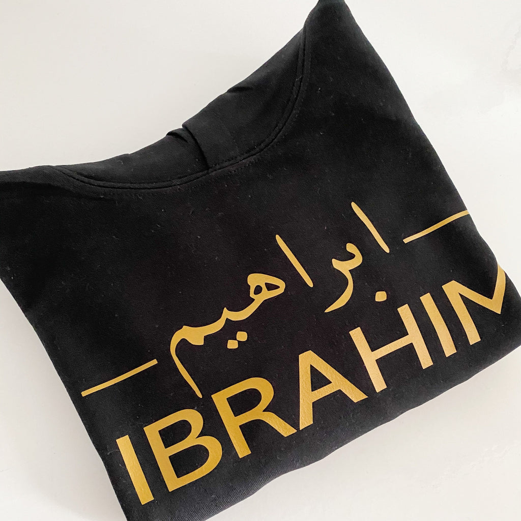 black hoodie with metallic gold Arabic and English name design printed across the chest