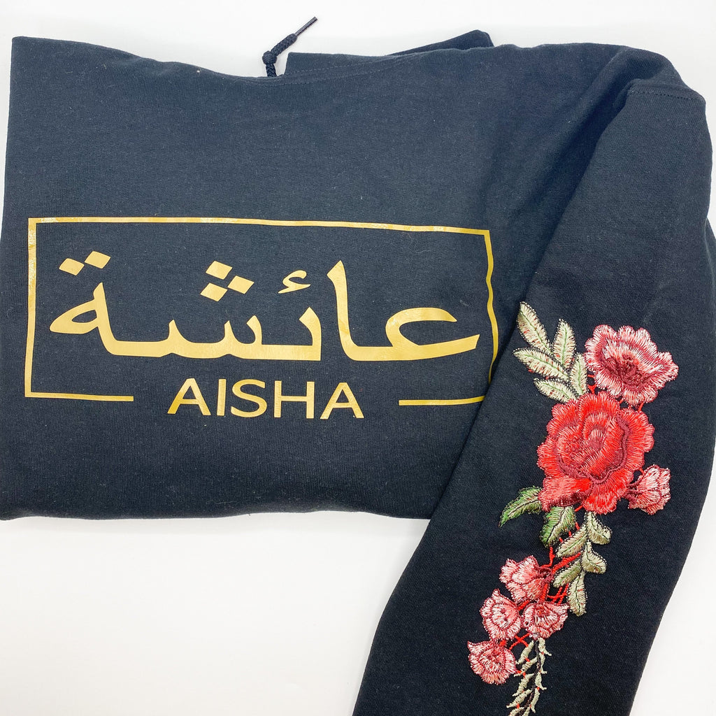 black hoodie with metallic gold Arabic and English name and red floral sleeve embroidery