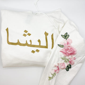 white sweatshirt with metallic gold Arabic name and pink floral sleeve embroidery
