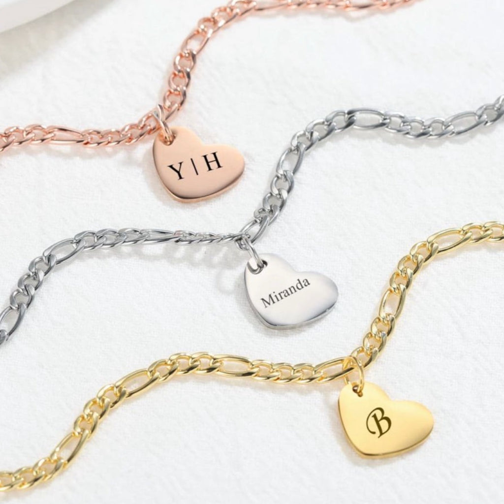 Adorn your ankles with love - our Engraved Heart Charm Anklet is a stunning figaro chain anklet featuring a heart charm ready to be customized with initials, names, texts, icons, messages, and beyond. Express your unique style and cherish meaningful moments with this personalized anklet. Elevate your look with a touch of elegance and love. 